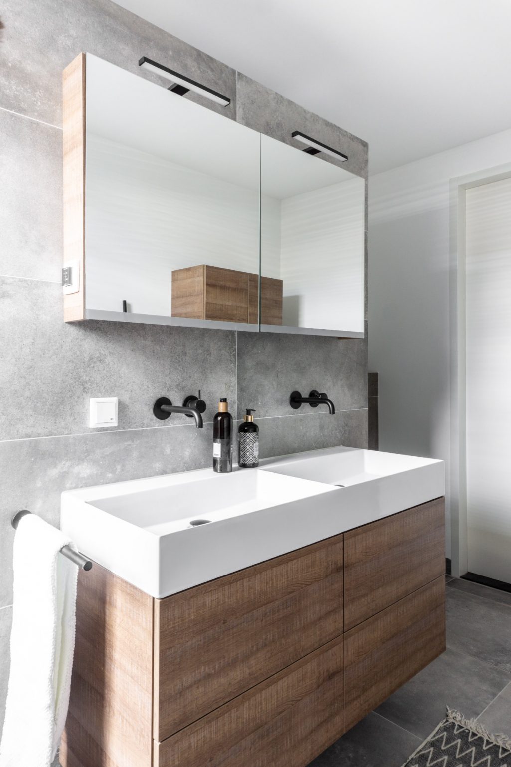 Scandinavische badkamer met grote grijze tegels, houten kastjes en witte waskommen | Stek Magazine